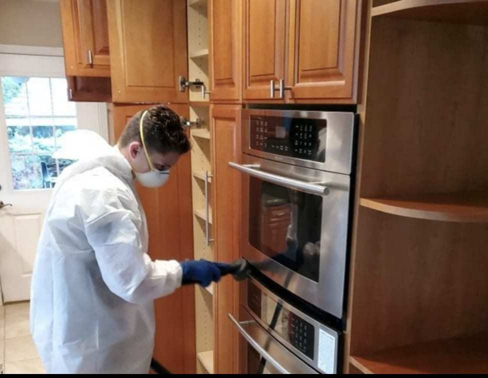 Technician in a protective suit cleaning the inside of a kitchen wall oven